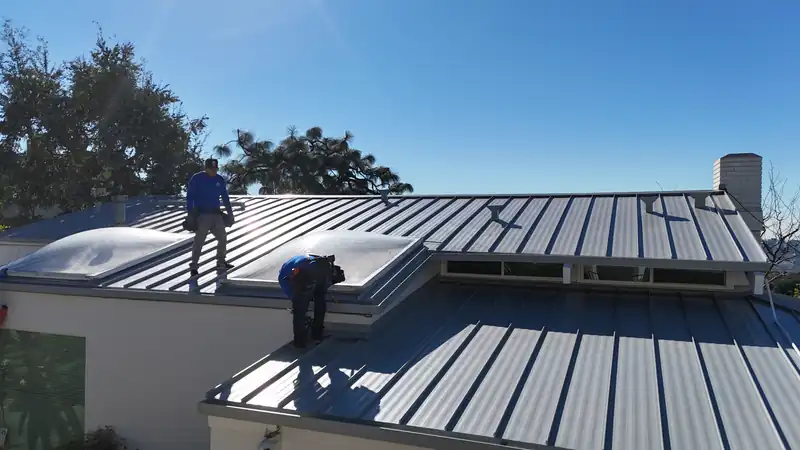Crew finishing a light gray standing seam roof around two dome skylights on a sunny day