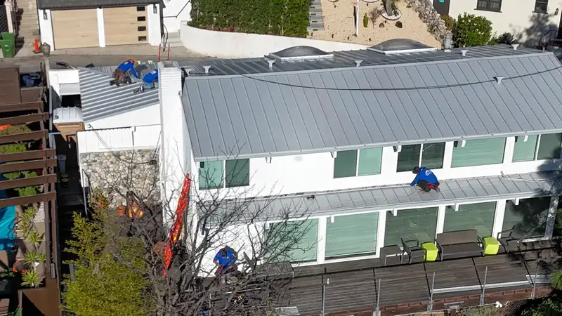 Crew installing standing seam panels on a white two-story hillside house