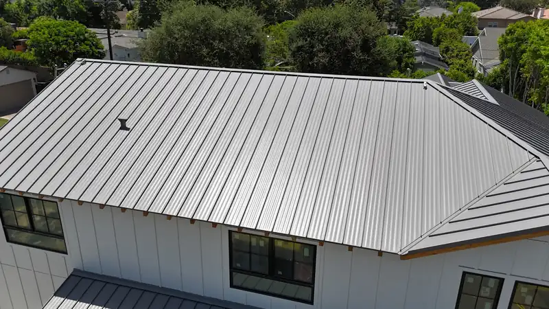 Gray standing seam metal roof with long straight panels and a hip roof over a white board-and-batten house