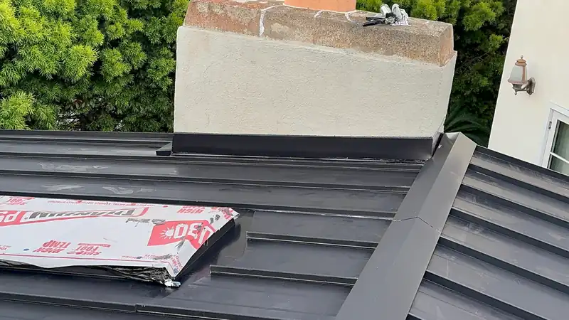 Black standing seam panels with a formed metal flashing around a chimney, during installation