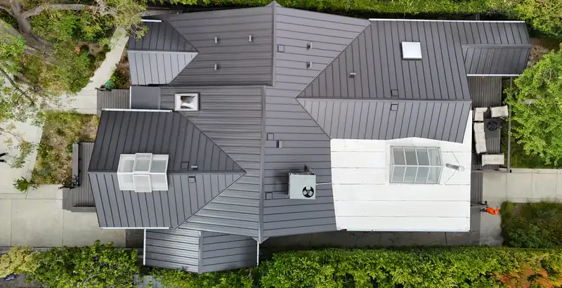 Top-down view of a dark gray standing seam metal roof with many hips, valleys and skylights