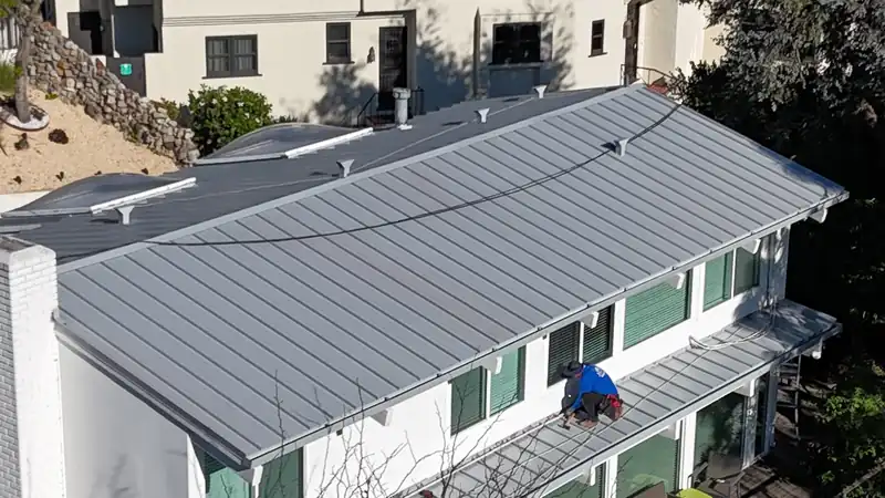 Light gray standing seam metal roof on a white two-story house with green shutters